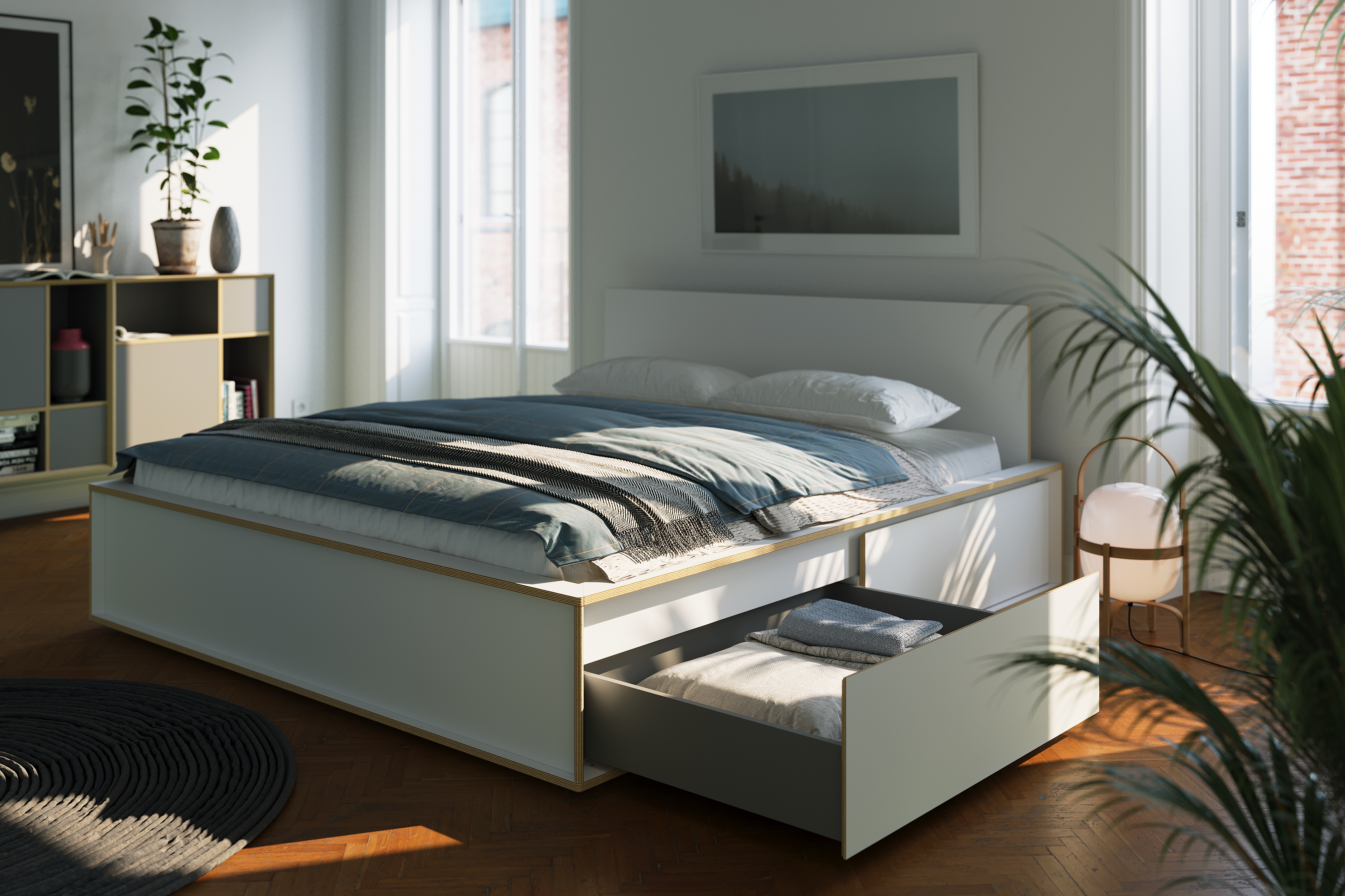 Das Spaze Doppelbett weiß mit Bettkasten mit großen Schubladen mit viel Platz für Bettwäsche und Tagesdecken steht hier in einem modernen sonnigen Schlafzimmer mit Parkettboden und einem Sideboard im Hintergrund.
